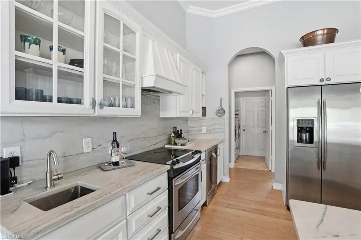 Kitchen featuring stainless steel appliances, white cabinets, premium range hood, glass insert cabinets, and light stone countertops