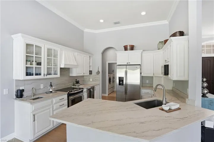 Kitchen with a peninsula, stainless steel appliances, premium range hood, white cabinetry, and glass insert cabinets