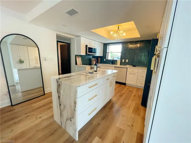 Kitchen featuring white cabinetry, a raised ceiling, light stone countertops, dishwasher, and light wood-style floors