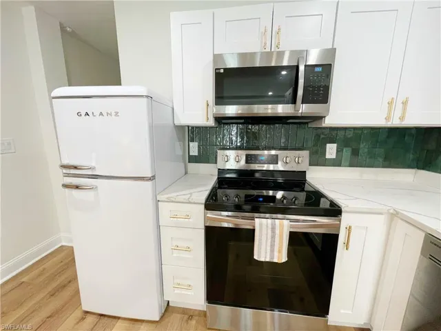 Kitchen with stainless steel appliances, white cabinetry, tasteful backsplash, and light stone counters
