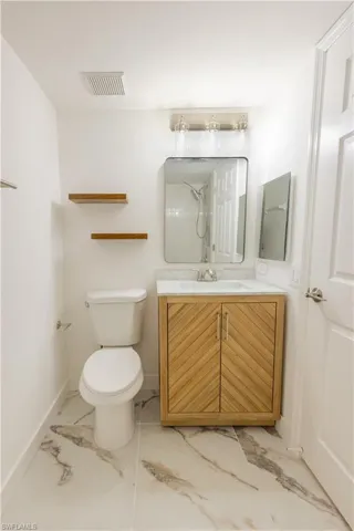 Full bath with toilet, visible vents, vanity, baseboards, and marble finish floor