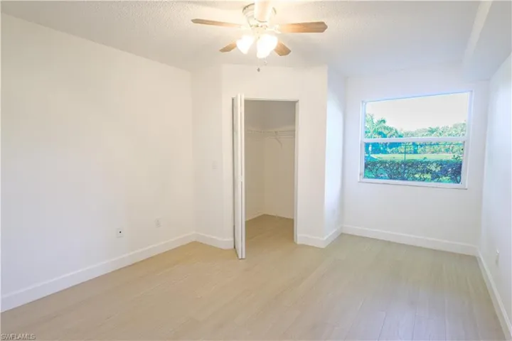 Unfurnished bedroom featuring a textured ceiling, light wood-style flooring, baseboards, a closet, and a walk in closet