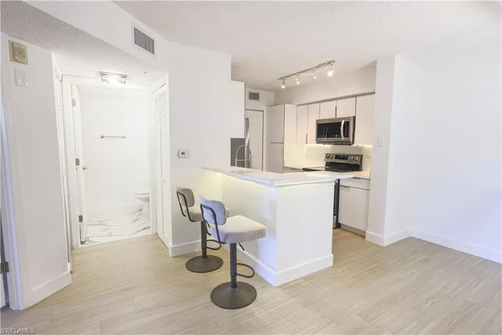 Kitchen featuring stainless steel appliances, a peninsula, visible vents, white cabinetry, and light countertops