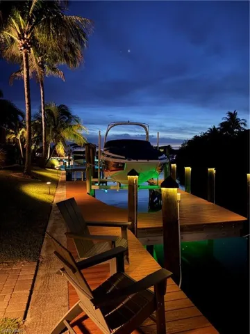Waterfront property featuring a private boat lift, a wood-finish dock with integrated lighting, and mature palm trees