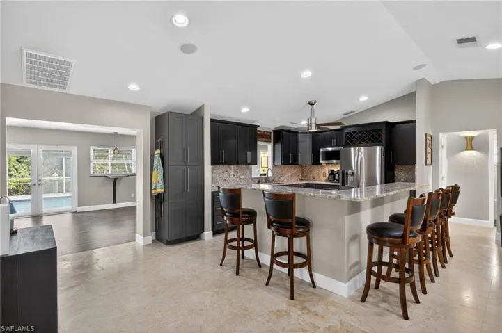 Kitchen featuring a kitchen bar, light stone counters, stainless steel appliances, decorative backsplash, and dark cabinetry