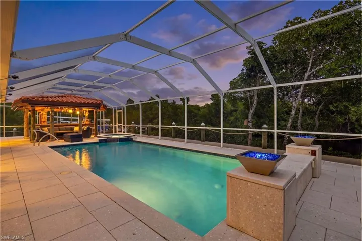 The property features a screened-in swimming pool area with a covered lounge space, an integrated spa, and tiled paving