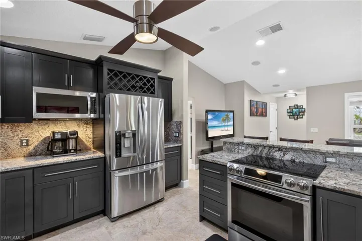 Kitchen featuring stainless steel appliances, vaulted ceiling, light stone countertops, ceiling fan, and backsplash