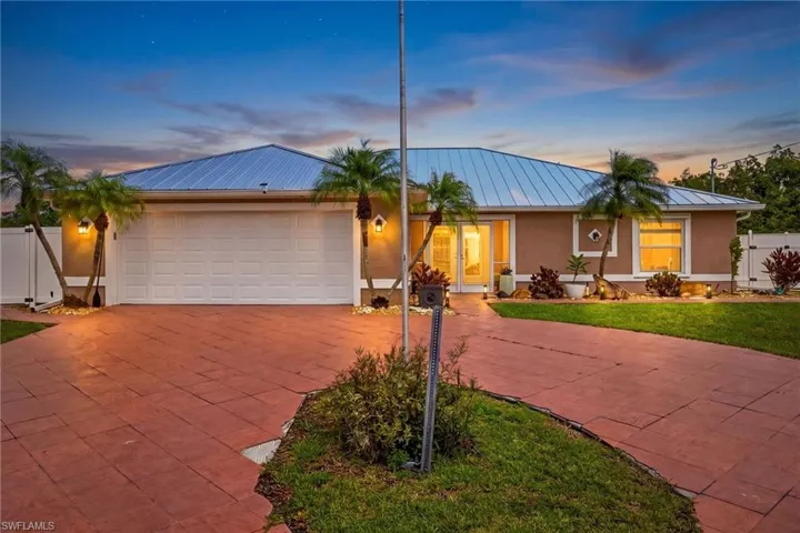 The property features a red paver driveway, a two-car garage, and a light blue metal roof