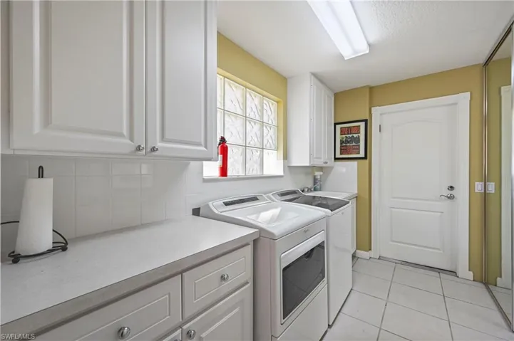 Laundry room featuring light tile patterned flooring, separate washer and dryer, and cabinet space