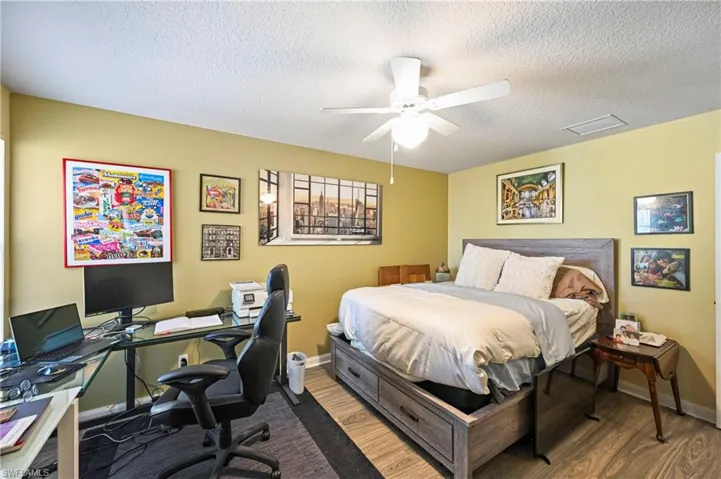 Bedroom with wood finished floors, a textured ceiling, a ceiling fan, and an office area