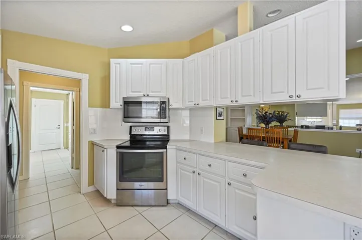 Kitchen with appliances with stainless steel finishes, white cabinetry, light countertops, light tile patterned floors, and a textured ceiling