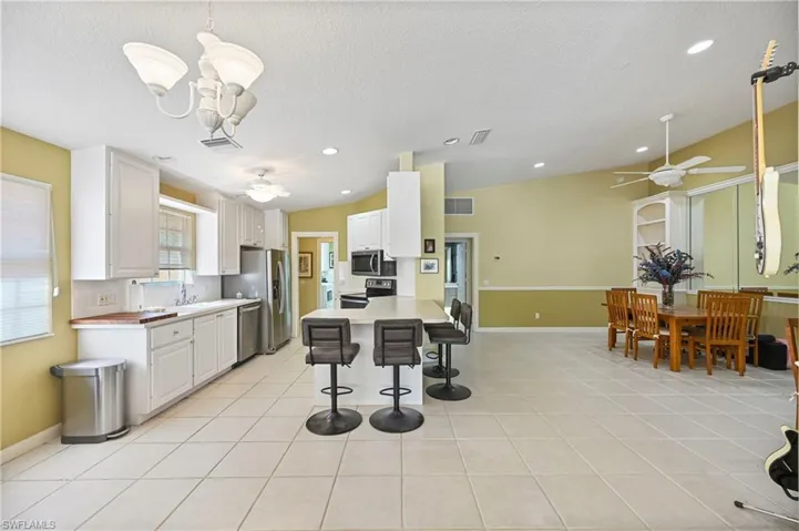 Kitchen featuring ceiling fan, a breakfast bar area, white cabinets, light tile patterned flooring, and recessed lighting