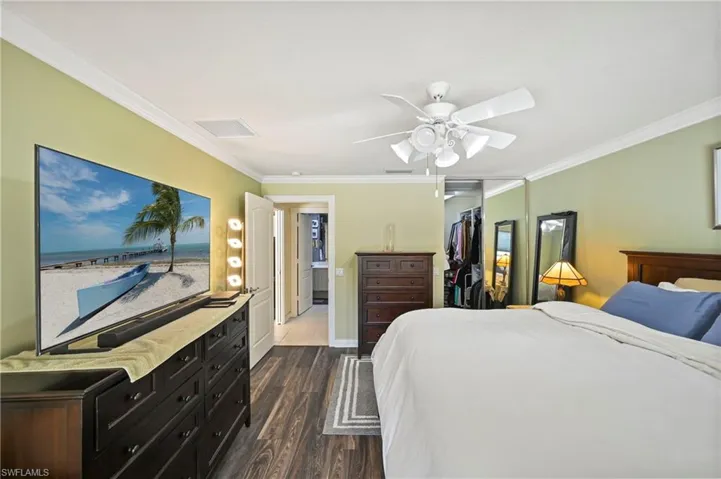 Bedroom featuring crown molding, dark wood-type flooring, ceiling fan, and a spacious closet