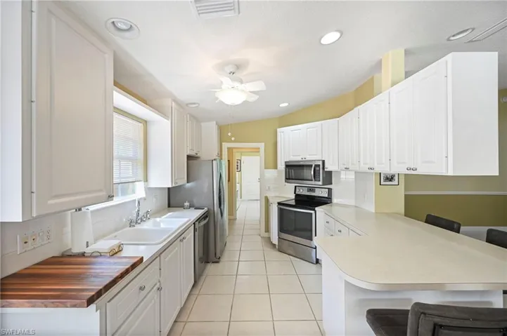 Kitchen with a kitchen bar, tasteful backsplash, appliances with stainless steel finishes, white cabinets, and recessed lighting