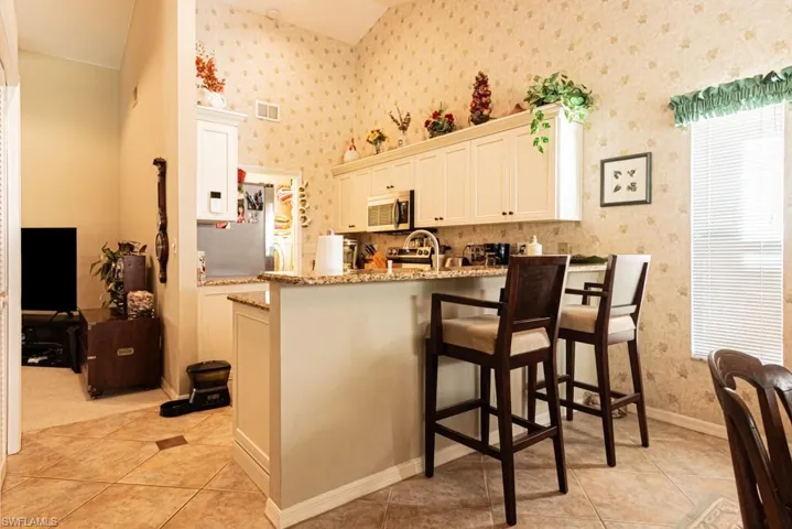 Kitchen with light stone countertops, white cabinets, light tile patterned floors, stainless steel microwave, and wallpapered walls