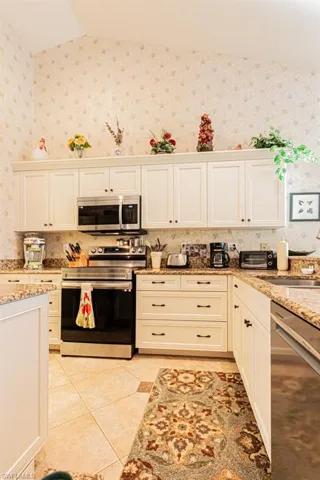 Kitchen with appliances with stainless steel finishes, light stone countertops, light tile patterned floors, white cabinets, and wallpapered walls