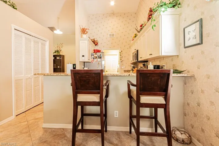 Kitchen with white cabinetry, light stone counters, light tile patterned floors, wallpapered walls, and a kitchen bar