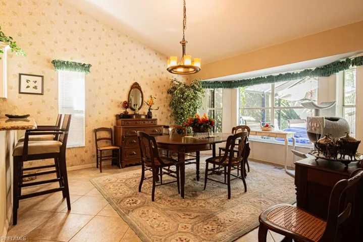 Dining area with light tile patterned floors, wallpapered walls, vaulted ceiling, and a chandelier