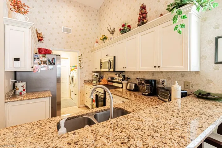 Kitchen featuring stainless steel appliances, light stone counters, white cabinets, wallpapered walls, and washer and clothes dryer