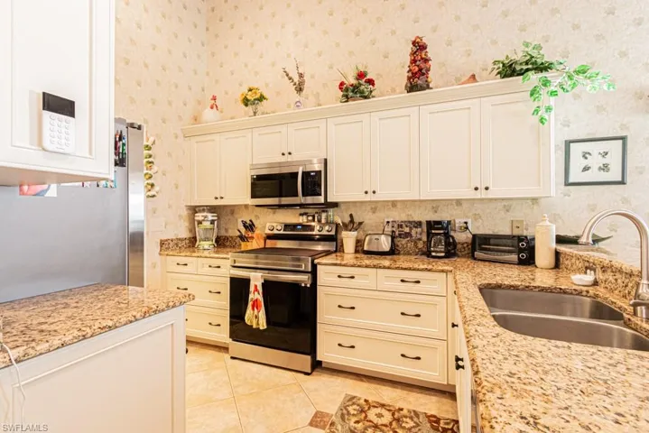 Kitchen featuring appliances with stainless steel finishes, light stone counters, light tile patterned flooring, backsplash, and wallpapered walls