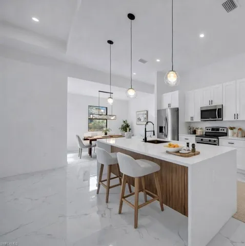 Kitchen with white cabinets, a kitchen breakfast bar, appliances with stainless steel finishes, an island with sink, and light stone countertops