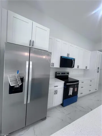 Kitchen with stainless steel appliances, white cabinets, light marble finish floors, and light stone counters
