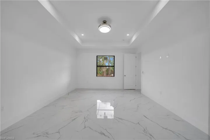 Empty room with light marble finish floors, recessed lighting, and a raised ceiling