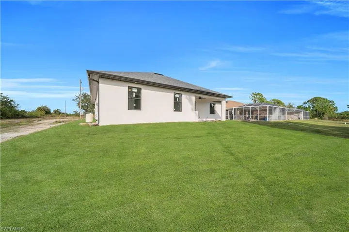 Rear view of property with a lawn, a patio area, a lanai, and stucco siding