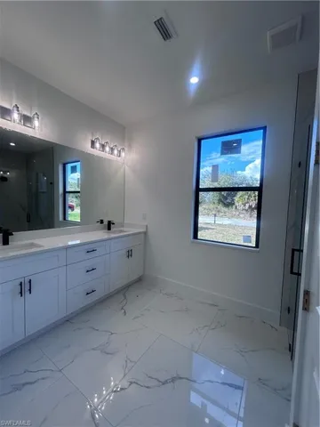 Full bath featuring a marble finish shower, double vanity, and light marble finish flooring