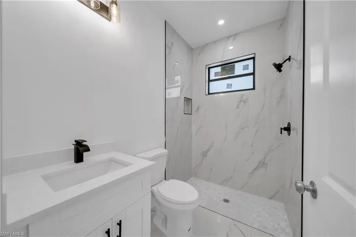 Bathroom featuring vanity, marble look tiles, a marble finish shower, and recessed lighting