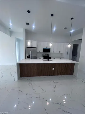 Kitchen featuring a large island with sink, white cabinets, refrigerator, light stone countertops, and black microwave