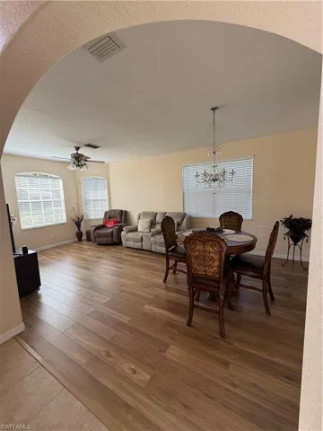 Dining area with wood finished floors, visible vents, arched walkways, a textured ceiling, and ceiling fan with notable chandelier