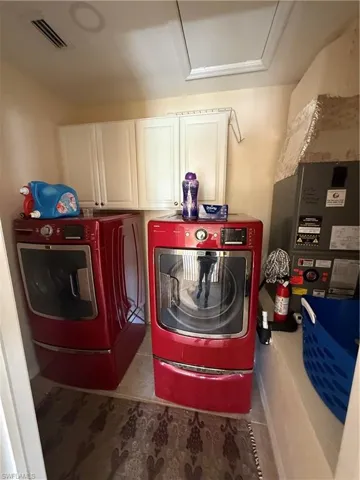 Laundry room featuring washer and clothes dryer, visible vents, cabinet space, and attic access