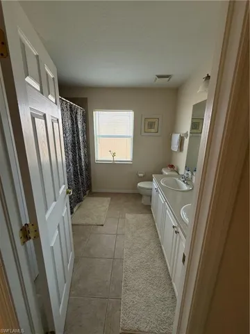 Bathroom featuring visible vents, double vanity, a sink, tile patterned flooring, and toilet