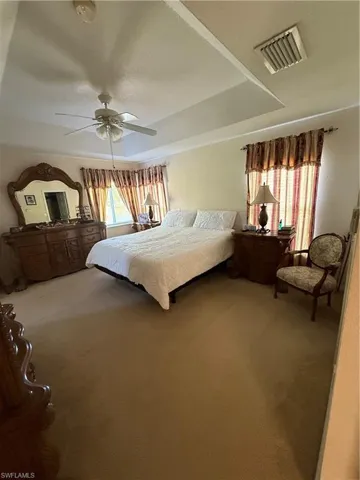 Carpeted bedroom featuring a raised ceiling, multiple windows, a ceiling fan, and visible vents