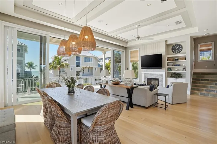 Dining area with a glass covered fireplace, built in shelves, light wood-style flooring, a tray ceiling, and a ceiling fan