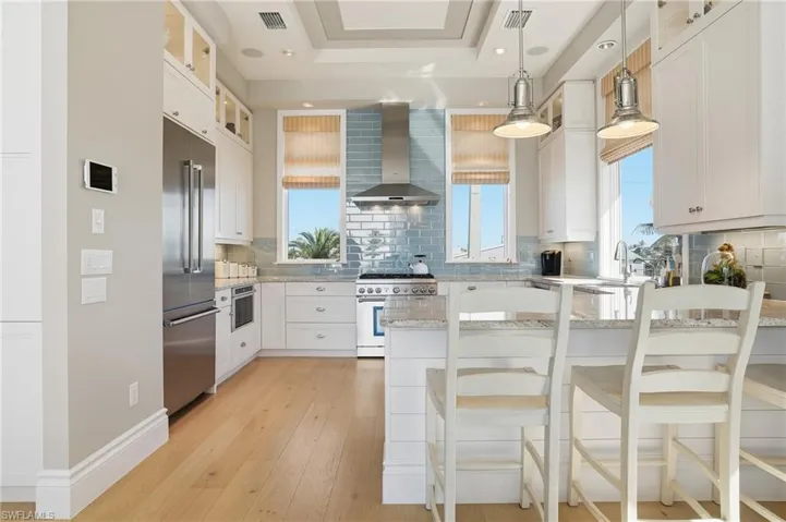 Kitchen with glass insert cabinets, white cabinetry, light stone countertops, and wall chimney exhaust hood