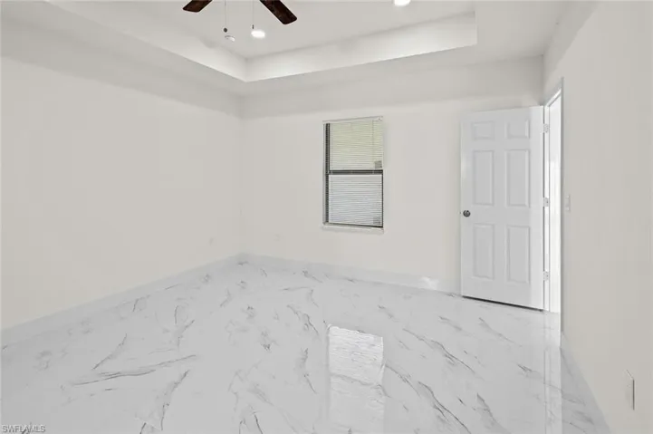 Empty room featuring ceiling fan, light tile floors, and a raised ceiling