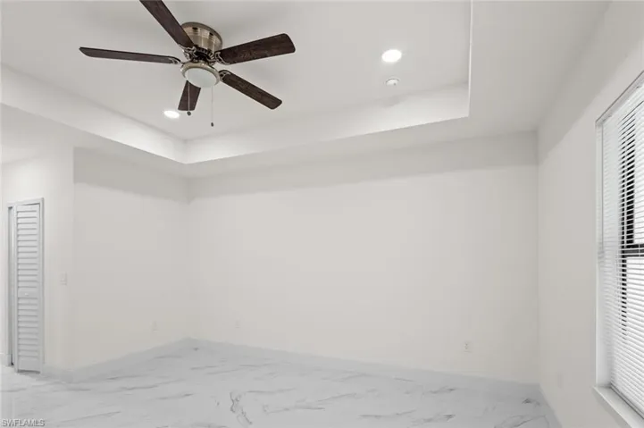 Tiled empty room featuring a healthy amount of sunlight, ceiling fan, and a tray ceiling
