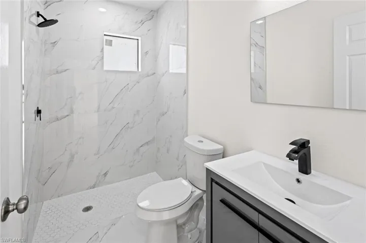 Bathroom featuring tiled shower, vanity, and toilet