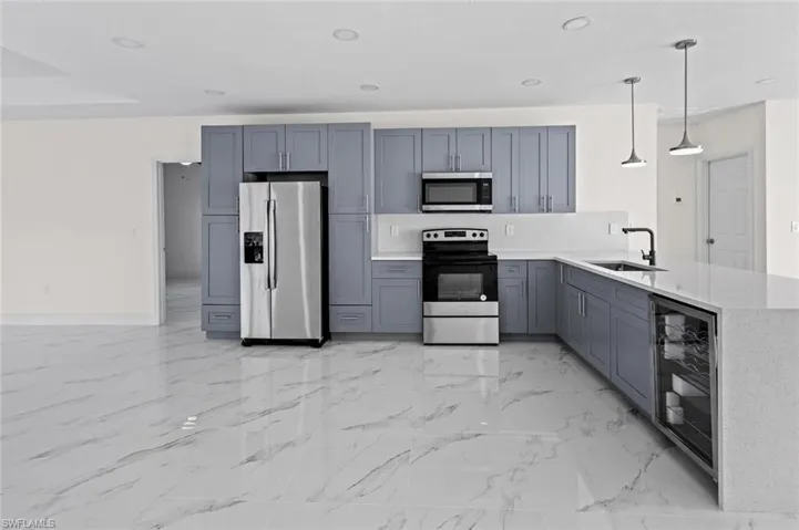 Kitchen with beverage cooler, kitchen peninsula, stainless steel appliances, light tile flooring, and sink