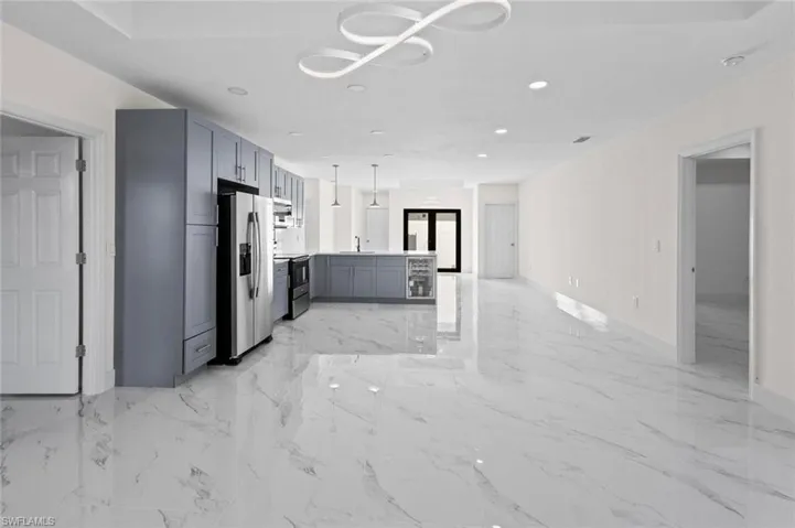 Kitchen featuring stainless steel refrigerator with ice dispenser, light tile floors, hanging light fixtures, gray cabinetry, and sink