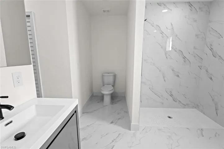 Bathroom featuring tiled shower, tile flooring, vanity, and toilet
