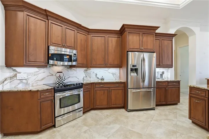 Kitchen with stainless steel appliances, fine wood cabinetry, granite counters, arched walkways, and tasteful stone backsplash