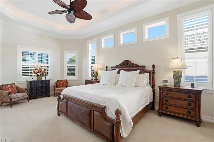 This spacious primary bedroom features a sitting area with soaring ceilings with custom lighting in the tray ceiling and plantation shutters
