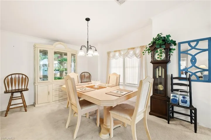 Dining area with a chandelier, vaulted ceiling, crown molding, and light colored carpet