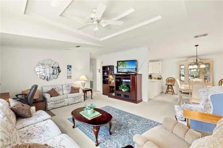 Living room with ceiling fan, light carpet, visible vents, and a raised ceiling