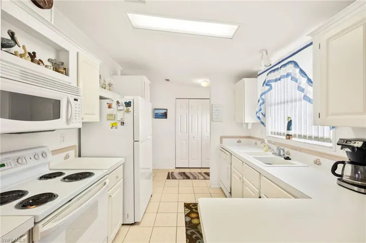 Kitchen with light tile patterned flooring, a sink, white appliances, and light countertops