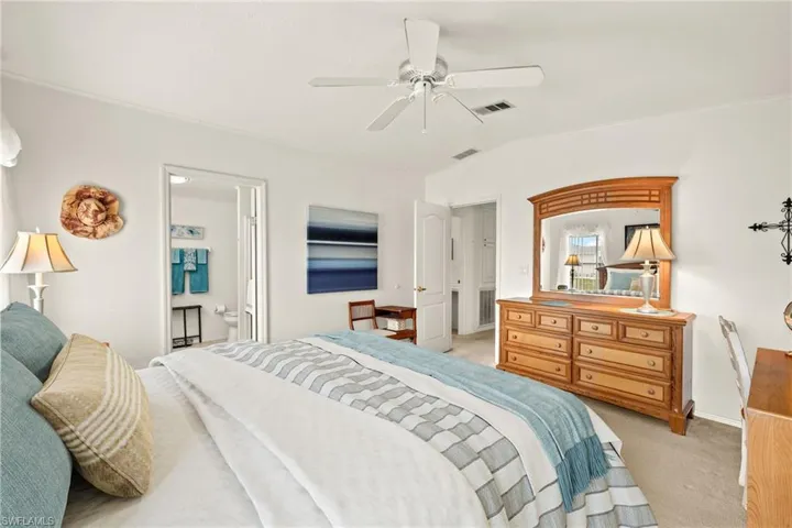 Bedroom with light colored carpet, visible vents, ensuite bathroom, and baseboards
