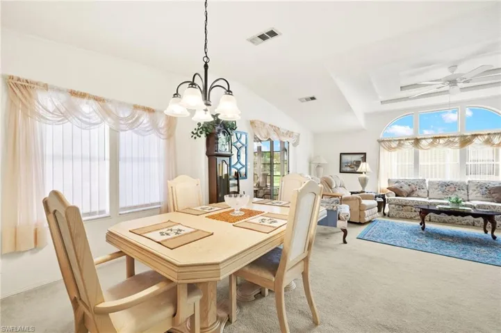 Dining room with ceiling fan with notable chandelier, visible vents, and light colored carpet